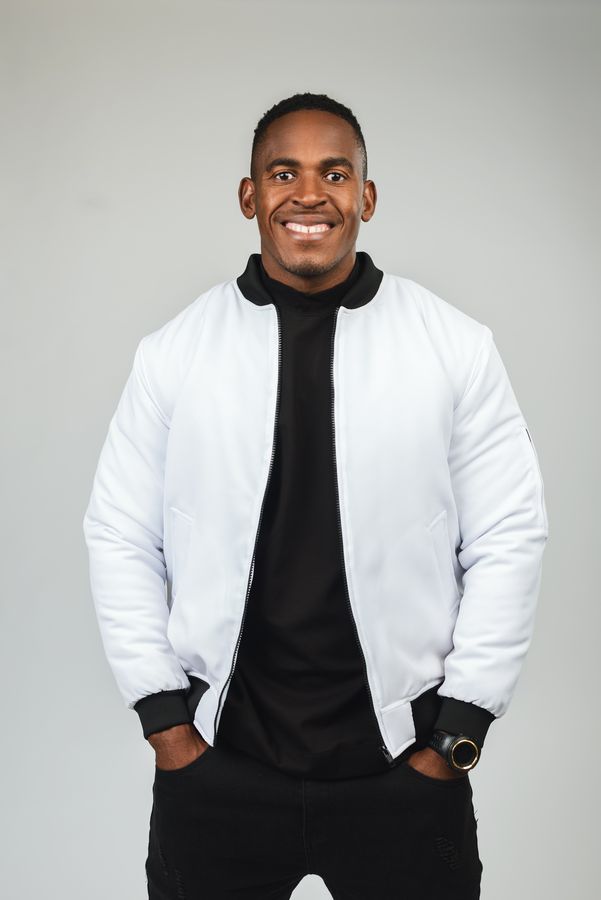 A man in a white bomber jacket against a grey studio backdrop