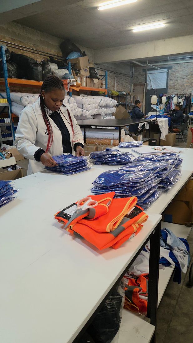 A quality checker in a lab coat folding finished garments at the packing table
