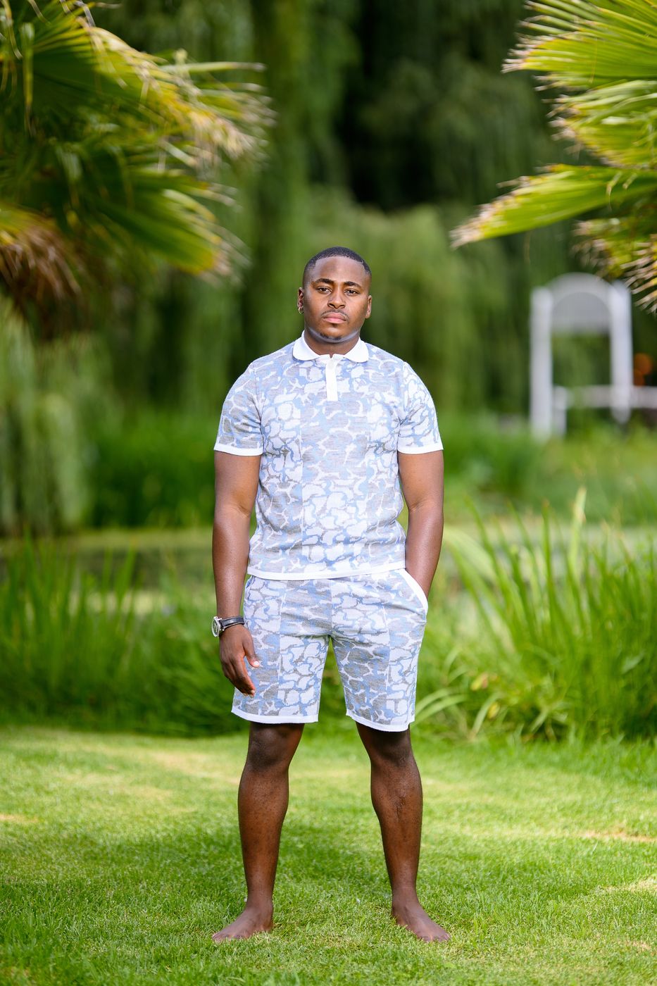 A man in a pale blue patterned polo and shorts set on a lawn