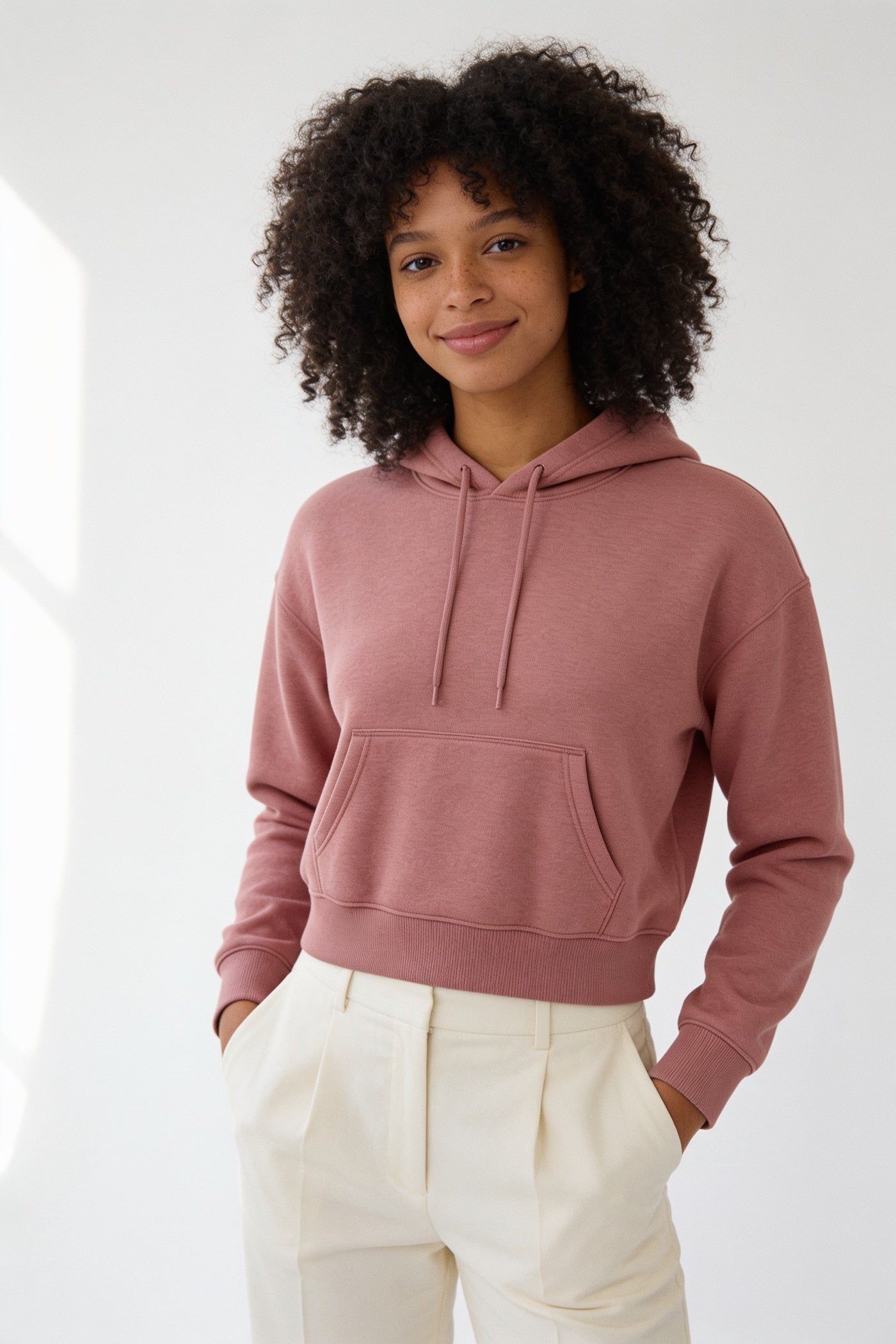 A young woman in a dusty pink hoodie in a bright studio
