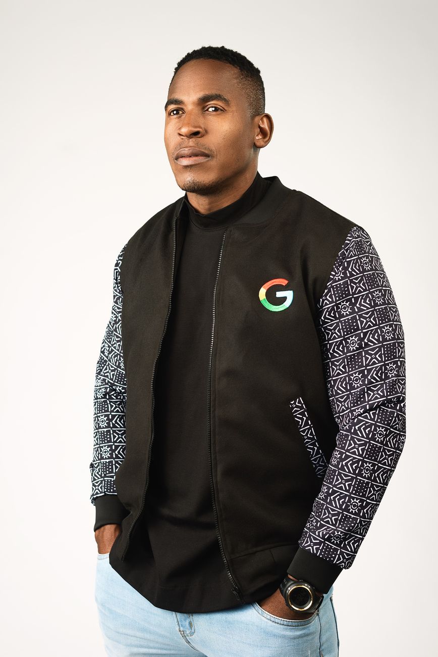 A man in a black bomber jacket with patterned sleeves and a Google logo