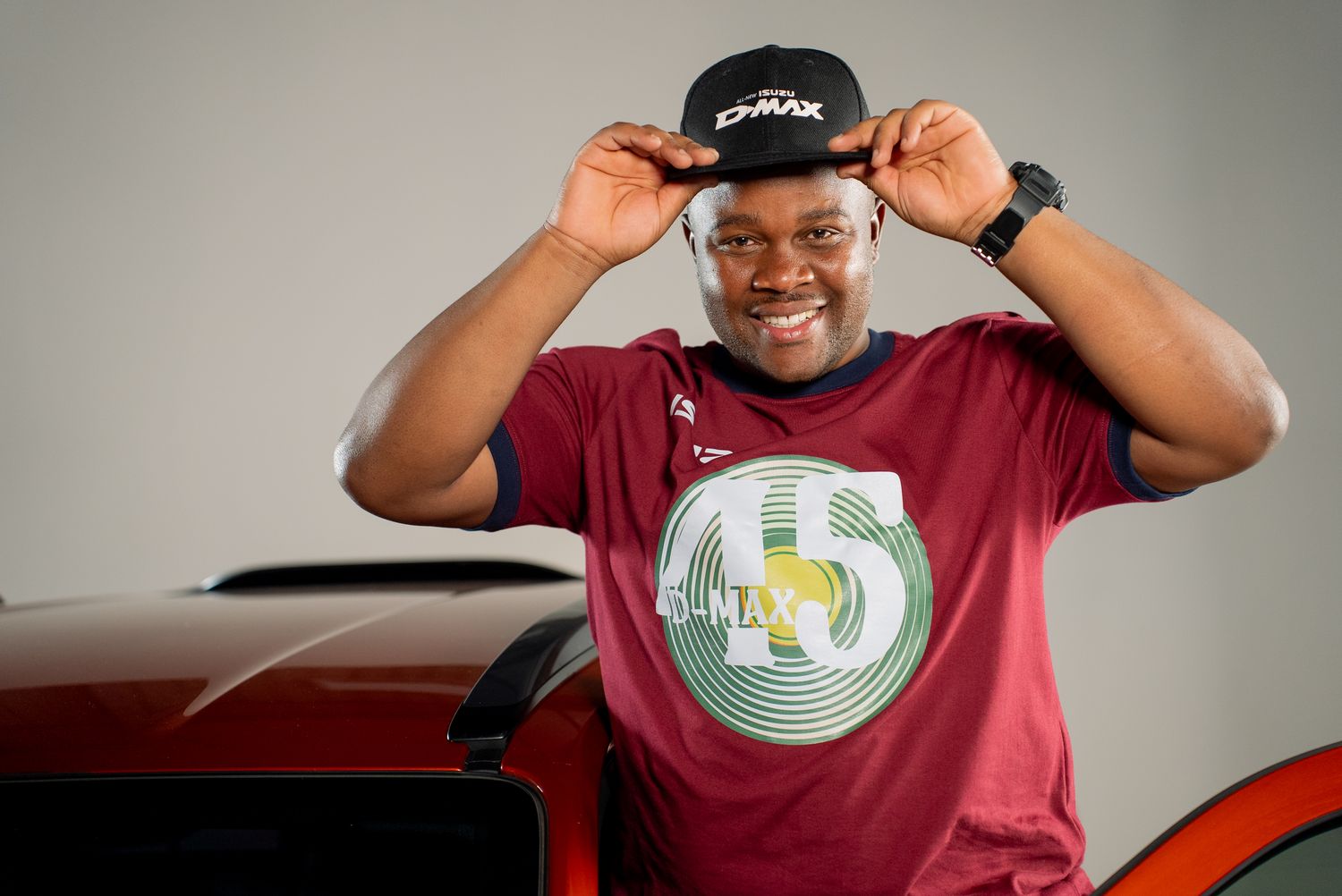 A man in a maroon jersey and cap beside a bakkie