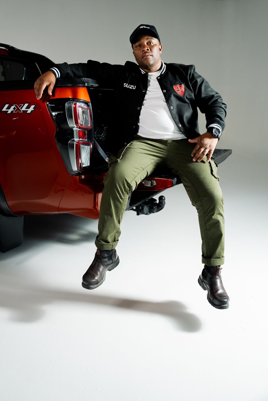 A man in an Isuzu varsity bomber leaning on a bakkie