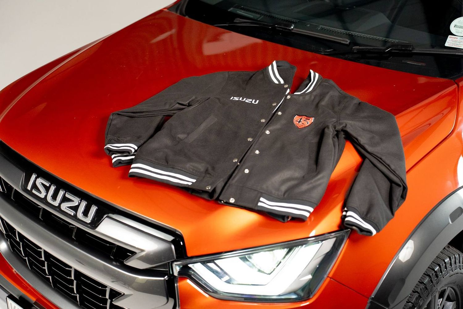 A black Isuzu varsity bomber laid on the bonnet of an orange D-Max