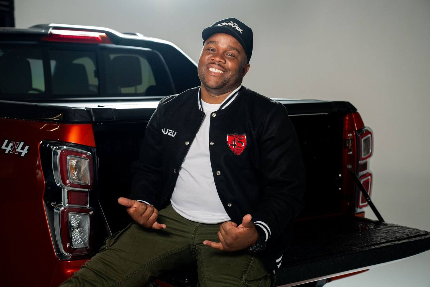 A smiling man in a black Isuzu varsity bomber sitting on a bakkie tailgate