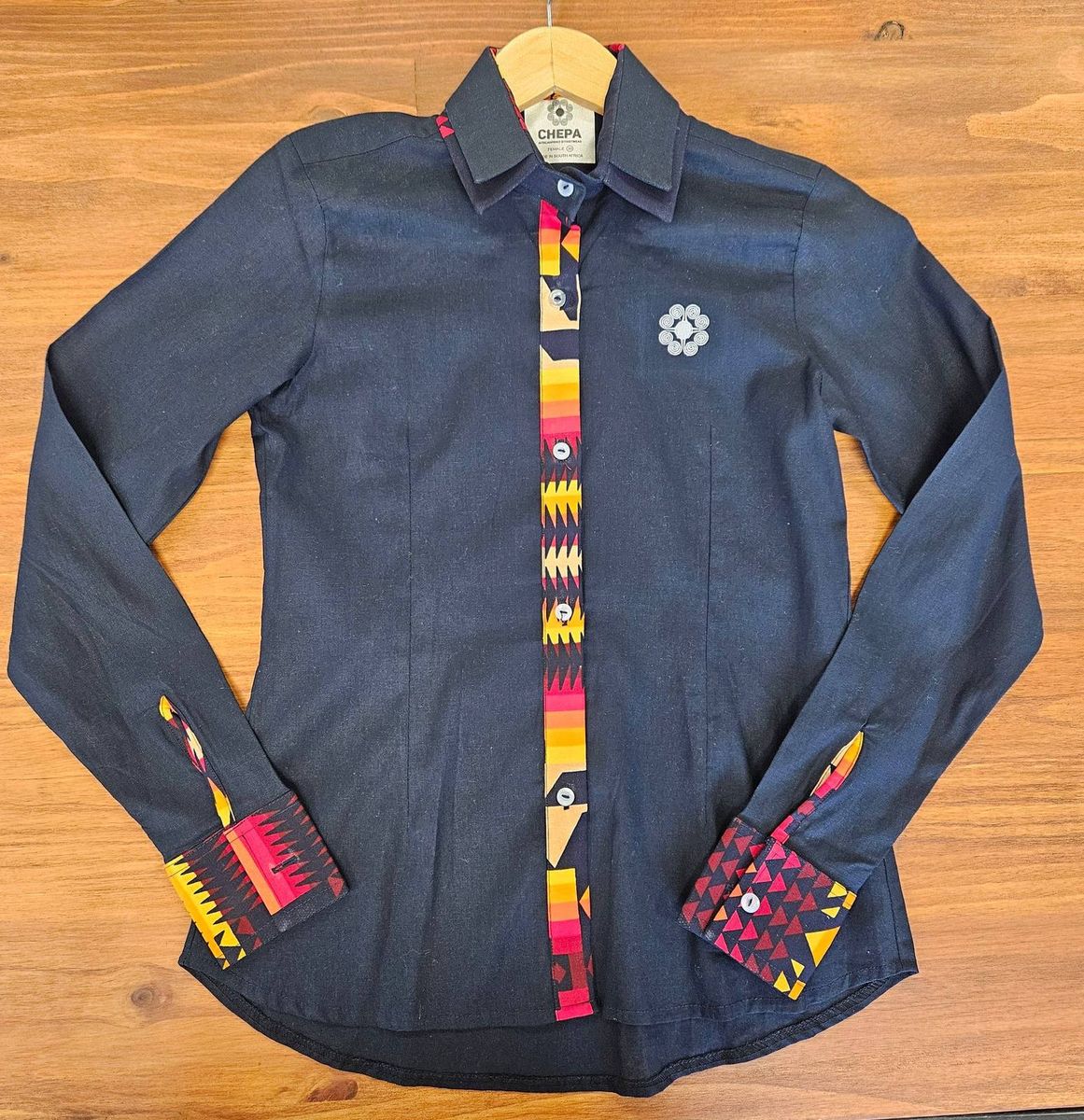 A navy shirt with a bright printed placket and cuffs on a hanger