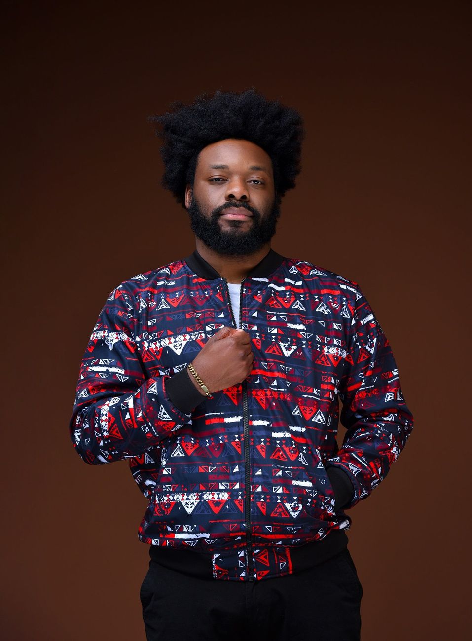 A man in a red, white and navy print bomber jacket on a dark backdrop